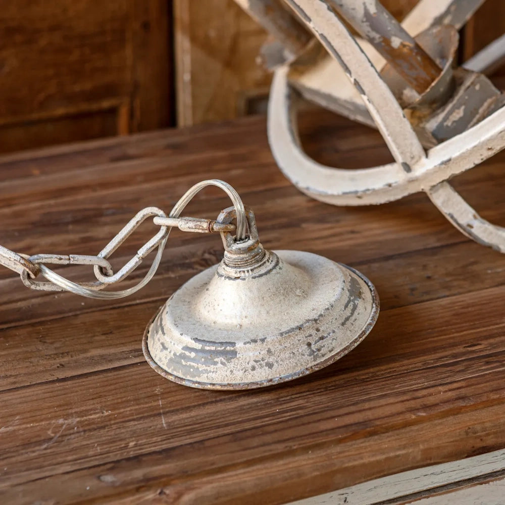 A close-up of a distressed, white-painted metal chandelier canopy with an attached hanging chain.