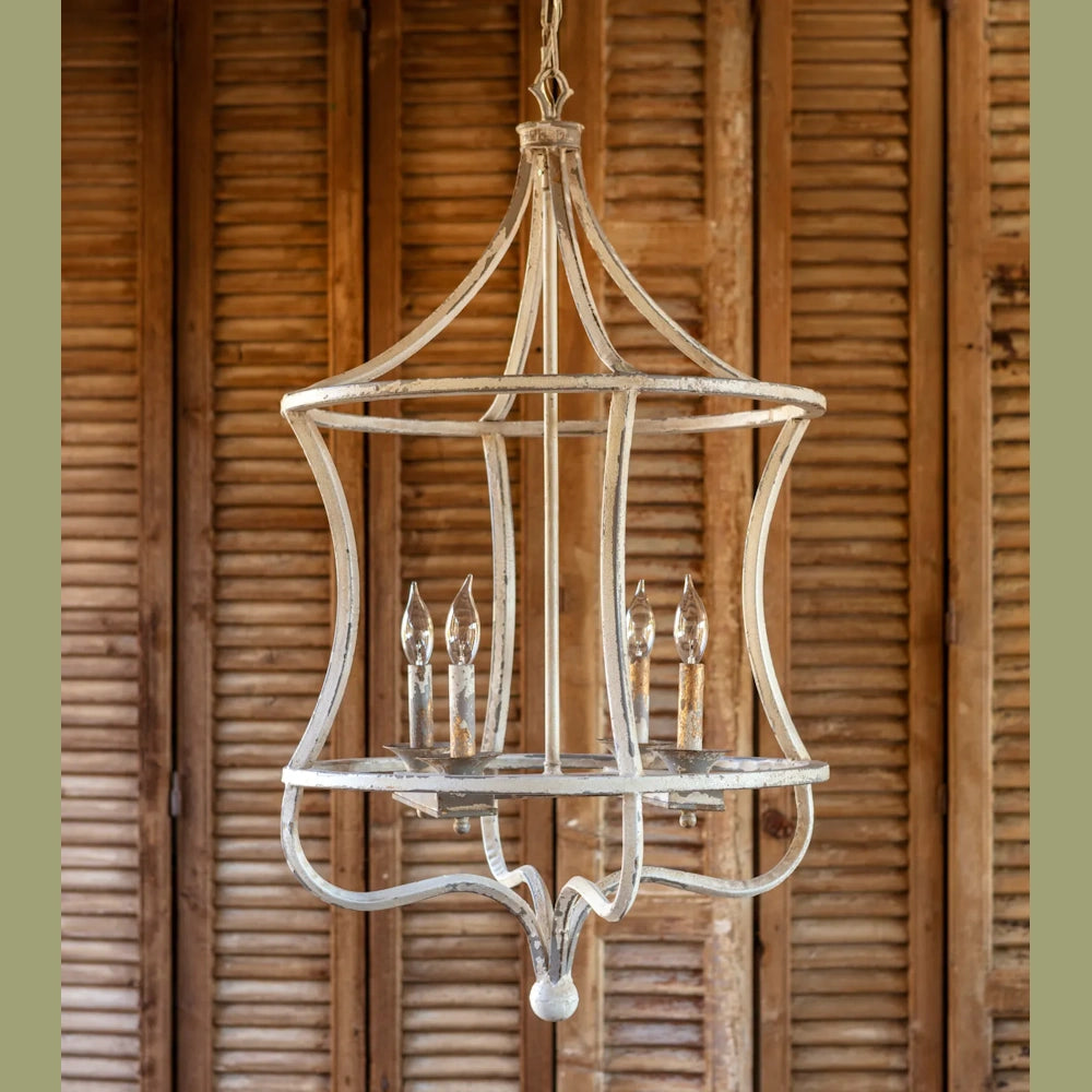 A rustic, distressed white lantern chandelier with four candle bulbs against a wood shutter background.