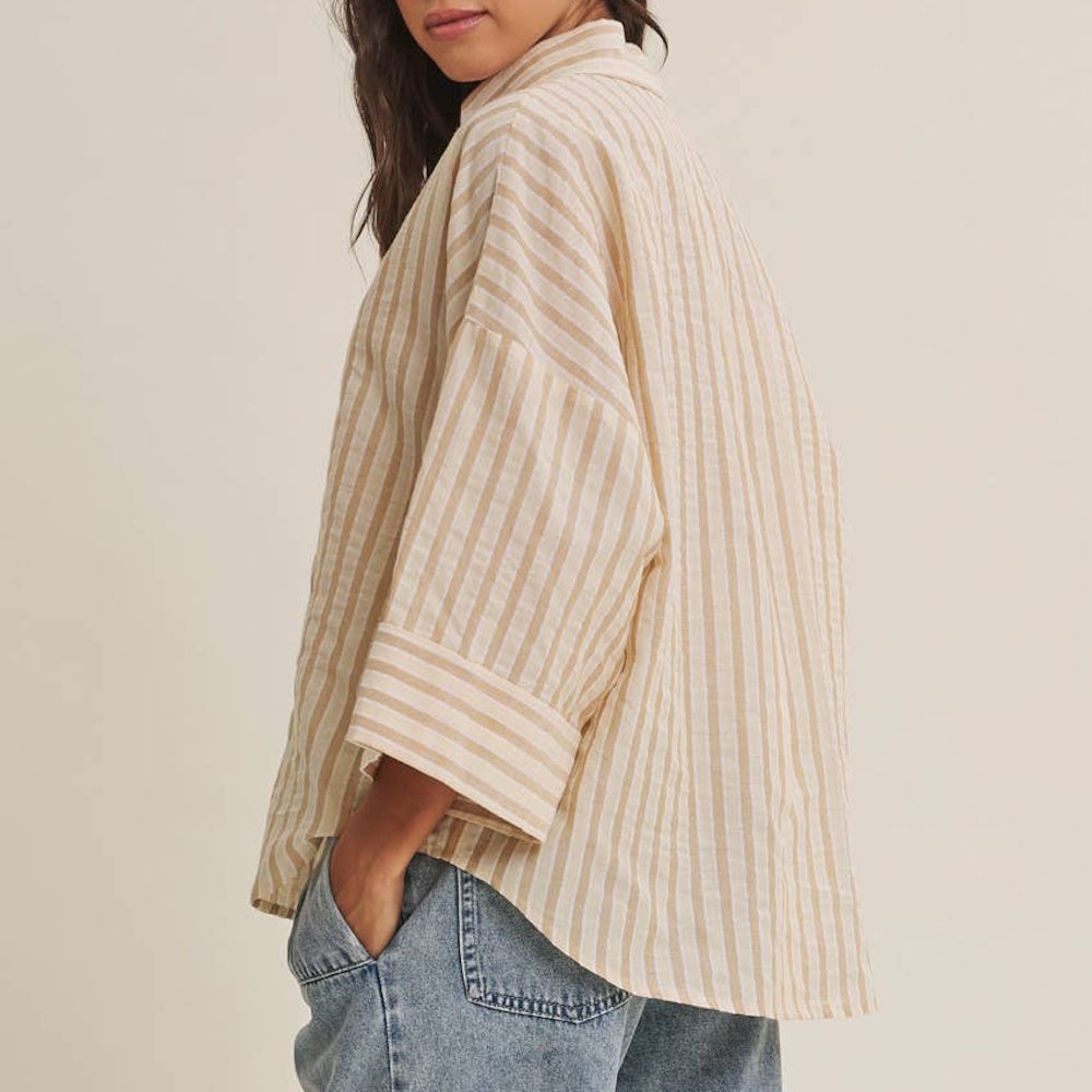 Side view of a relaxed beige-and-white striped short-sleeve button-down shirt paired with denim jeans.