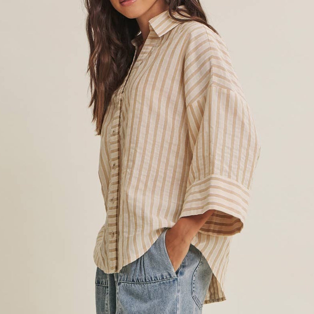 Side view of a woman wearing a tan and white striped button-down shirt with wide sleeves and blue jeans.