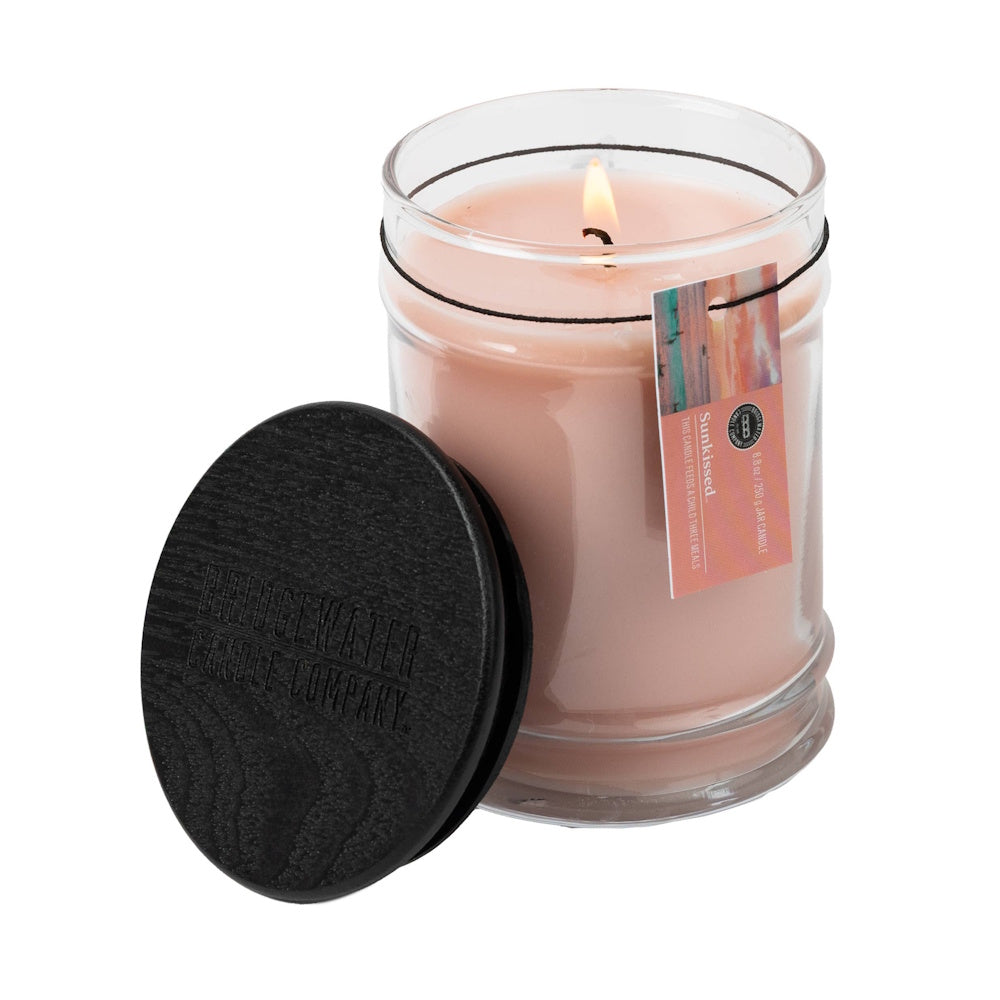 Bridgewater Candle Company Sunkissed 8.8 oz jar candle with lit wick and black wooden lid on white background.
