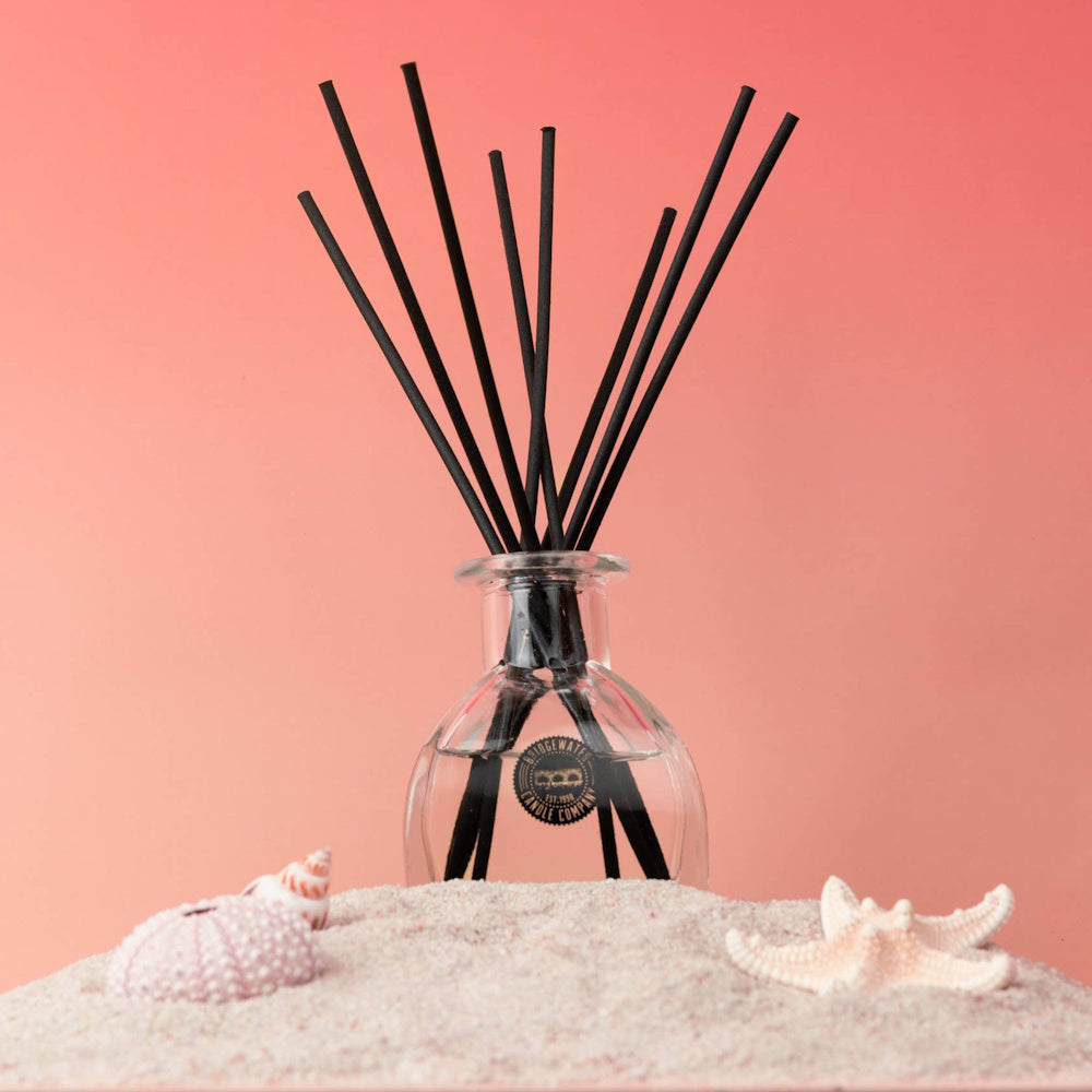 Bridgewater Candle Company reed diffuser in sand with starfish and seashells, beach-themed home fragrance decor.