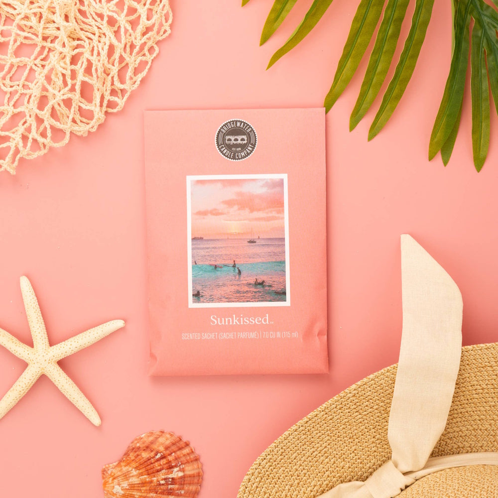 Bridgewater Candle Company Sunkissed scented sachet on pink background with starfish, seashell, and sun hat.