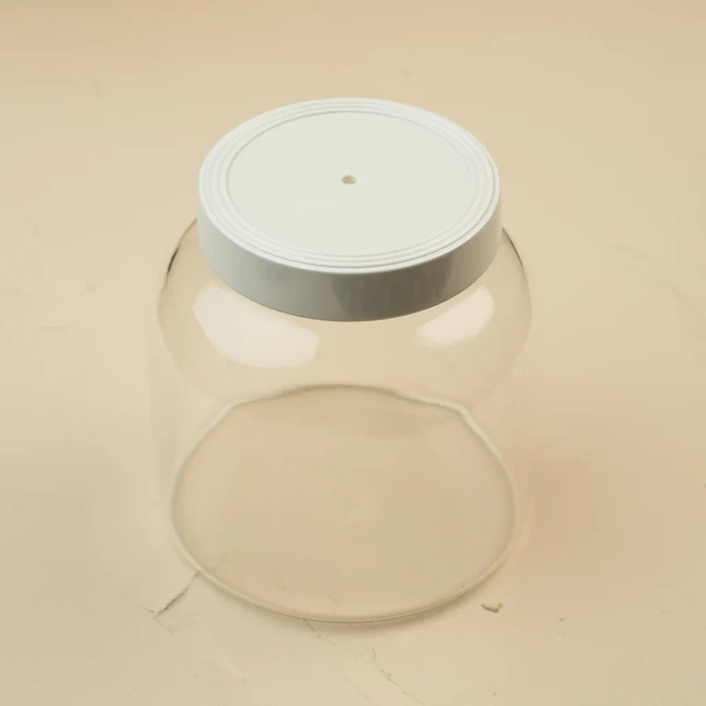 Clear glass jar canister with a white lid containing a small center hole, sitting on a neutral background.