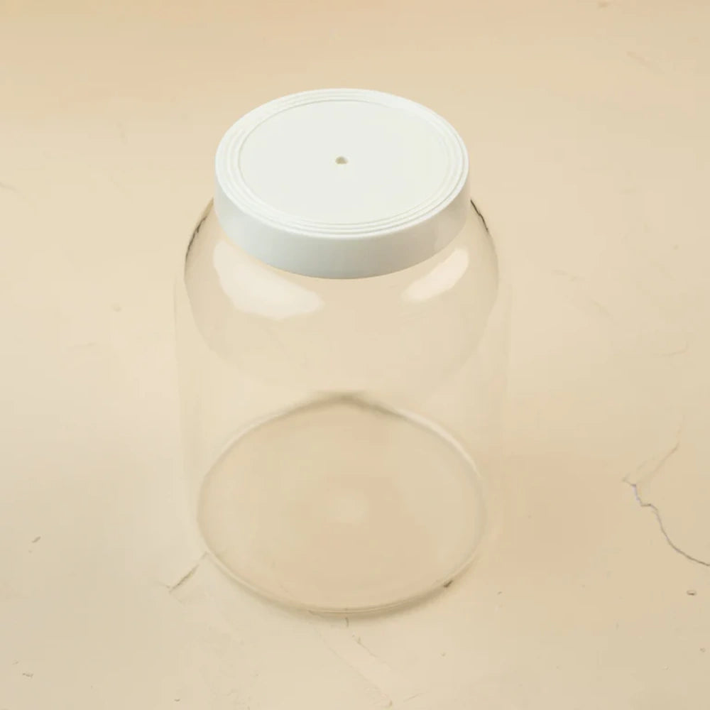 A clear glass storage canister topped with a white ceramic lid on a light beige surface.
