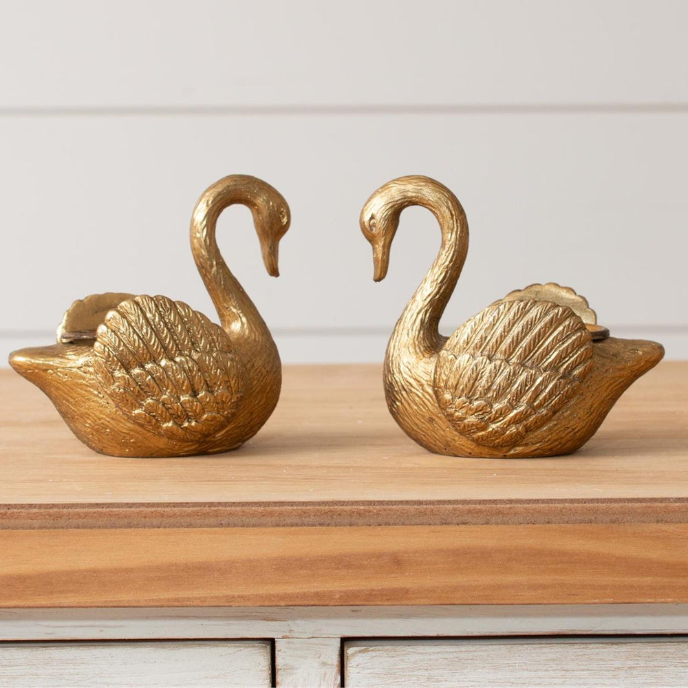 Pair of gold swan tapered candle holders with textured wings facing each other on a wooden surface.