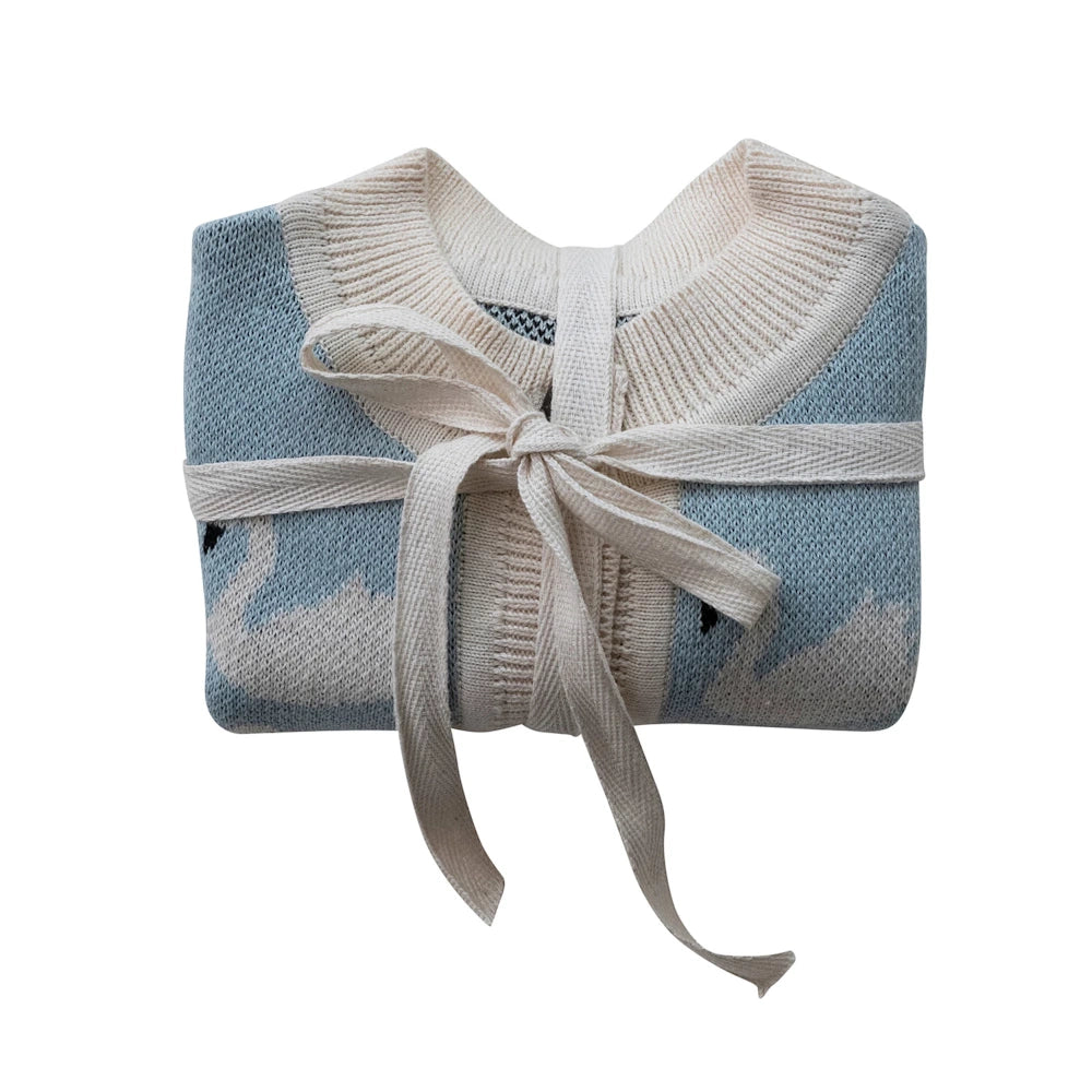 Folded light blue cotton knit baby cardigan with white swan pattern and cream ribbon bow.