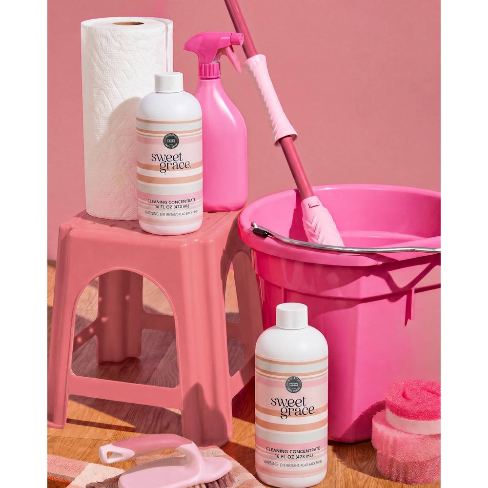 Sweet Grace Cleaning Concentrate bottles displayed with pink cleaning supplies, a stool, bucket, and mop.