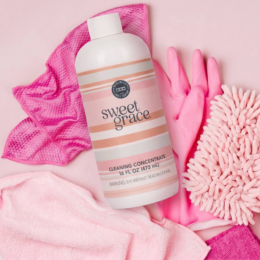 Bottle of Sweet Grace cleaning concentrate surrounded by pink cleaning cloths, gloves, and a duster.