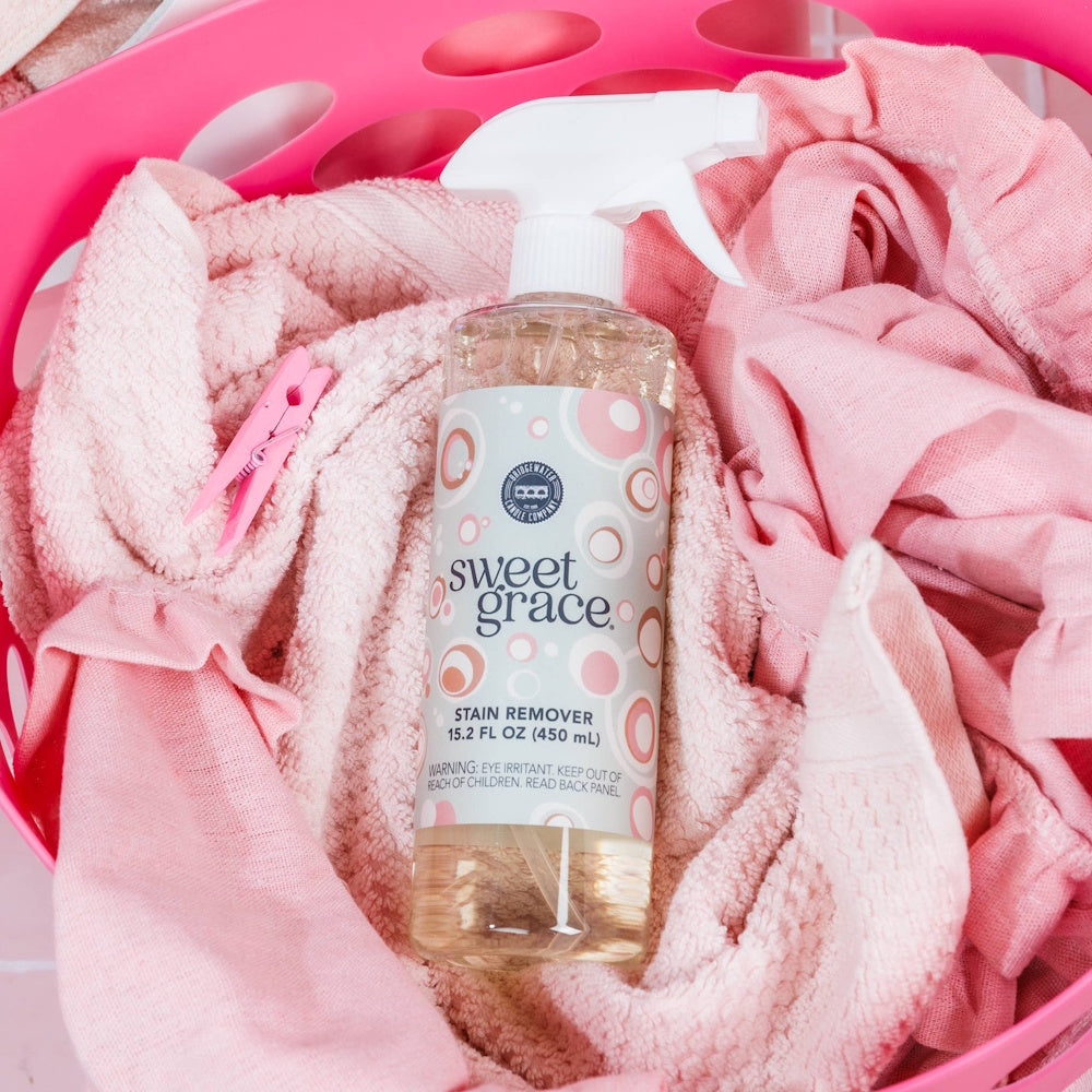 Sweet Grace Stain Remover spray bottle inside a pink laundry basket filled with soft pink towels.