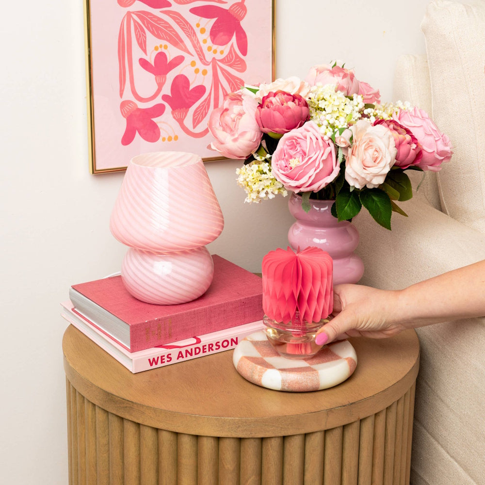 Hand placing a pink honeycomb diffuser on a coaster next to pink flowers and a stack of books.