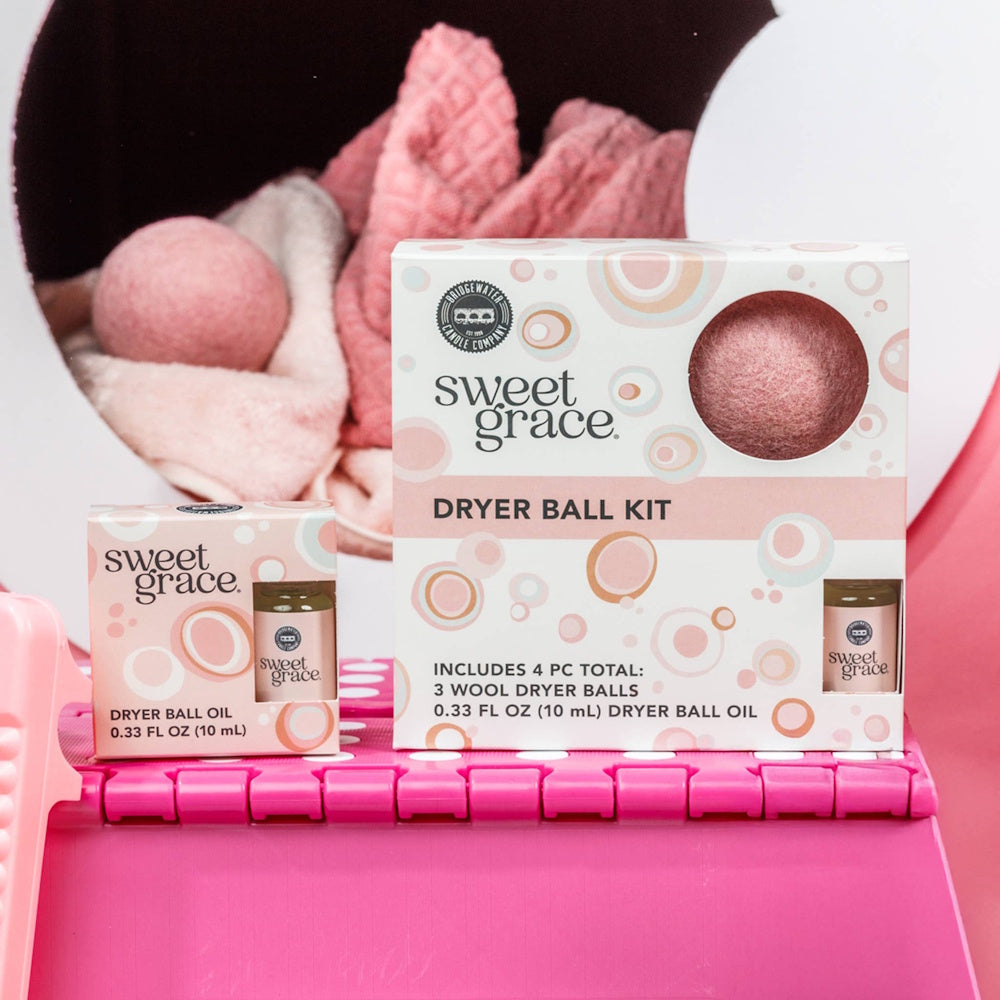 Sweet Grace Dryer Ball Kit and Dryer Ball Oil displayed in front of a dryer with pink laundry and dryer balls.