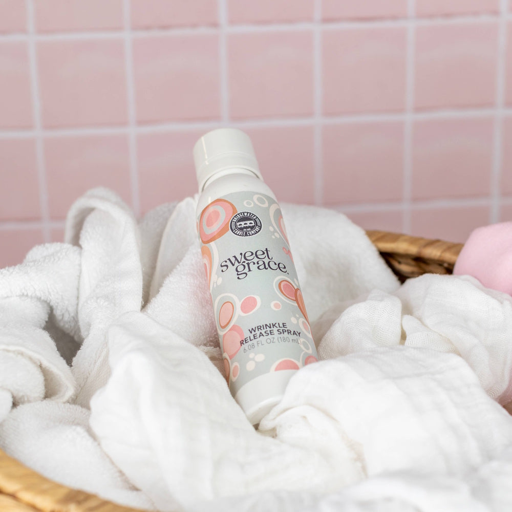 Sweet Grace wrinkle release spray bottle resting in a laundry basket with soft white towels.