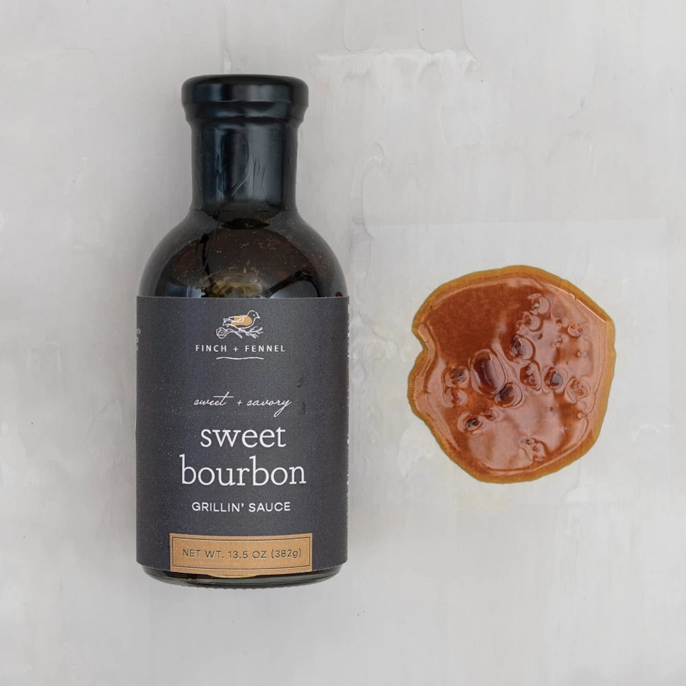 Finch + Fennel Sweet Bourbon Grillin’ Sauce bottle and a sauce sample on a white marble background.