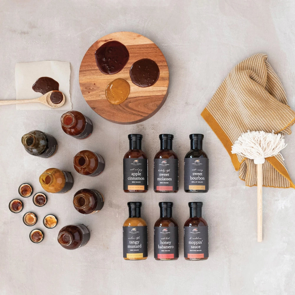 Flat lay of BBQ sauces, grilling tools, raw tomahawk steak, and roasted chicken on a light textured background.
