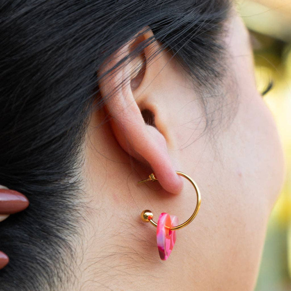 Woman wearing a gold hoop earring with a marbled pink resin heart charm.