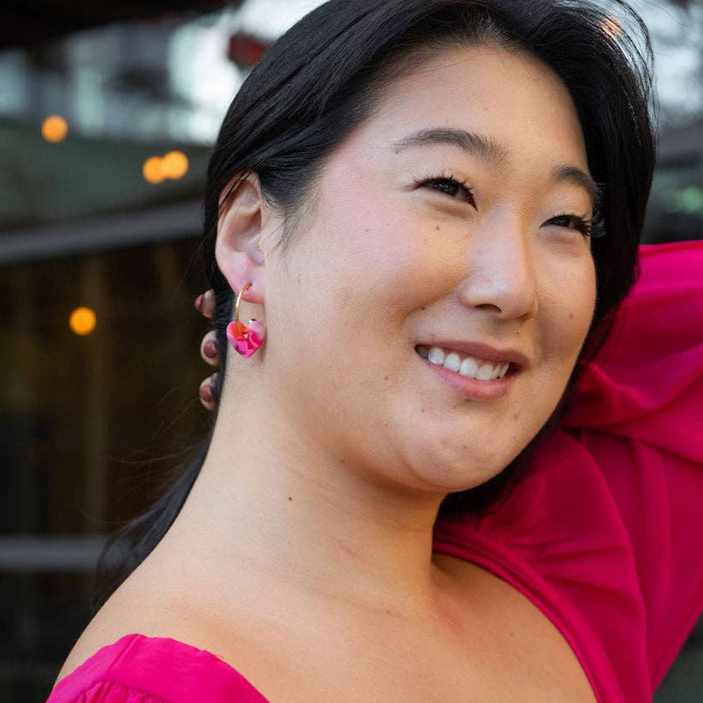 Woman wearing gold sweetheart hoop earrings with pink marble heart charms.