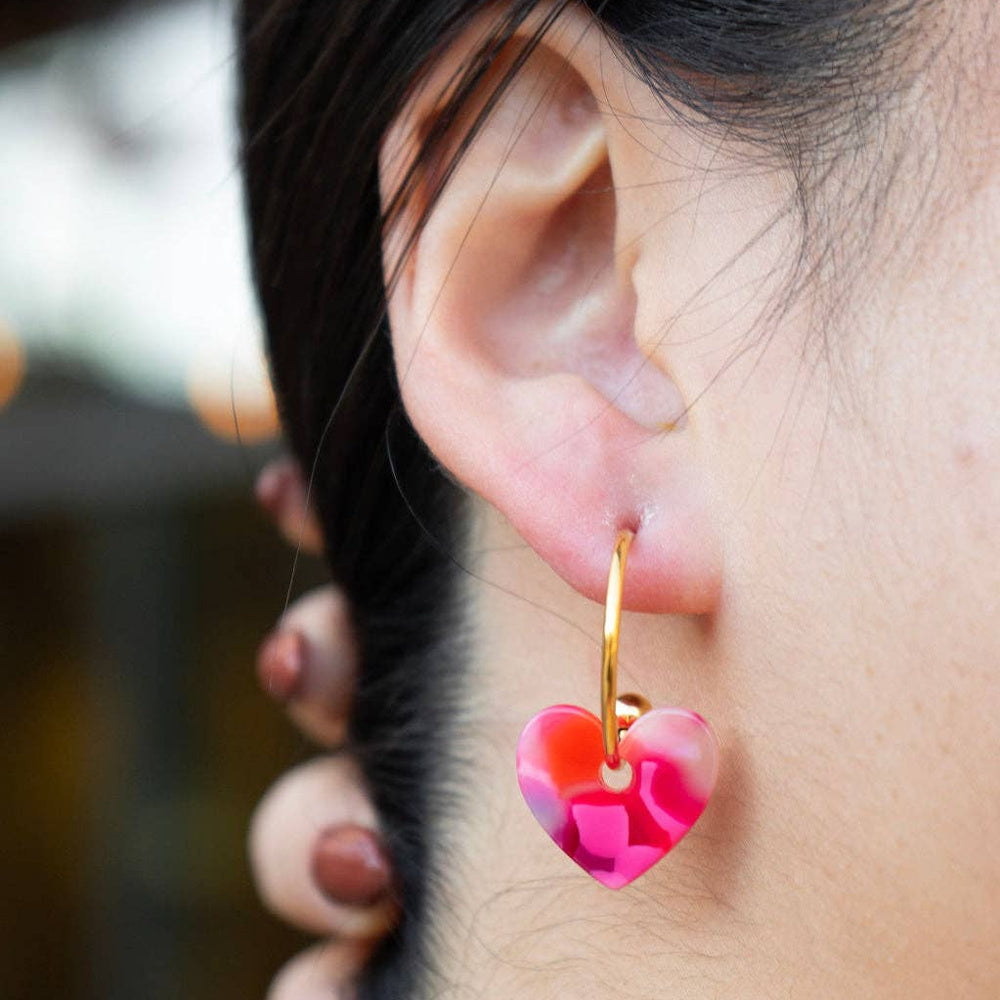 Model wearing gold Sweetheart Hoop earring with a vibrant pink translucent resin heart charm.