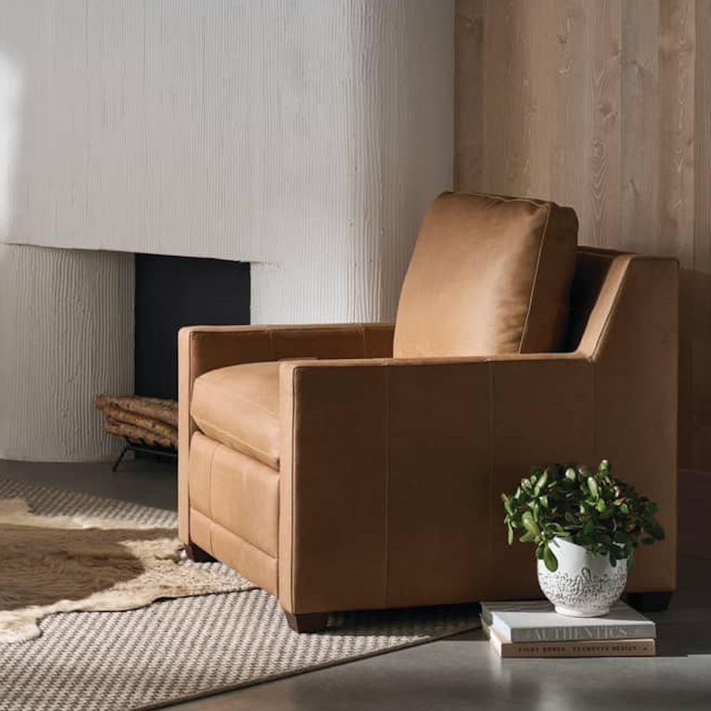 Modern tan leather recliner chair in a minimalist living room with a fireplace and potted jade plant.