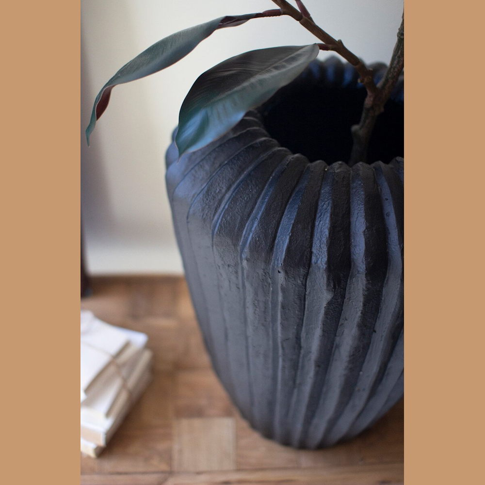 Black fluted composite stone urn in matte black finish holding a plant on a wooden surface.