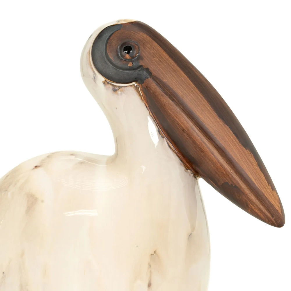 Close-up of a ceramic pelican figurine featuring a glossy cream neck, dark eye, and large brown beak.