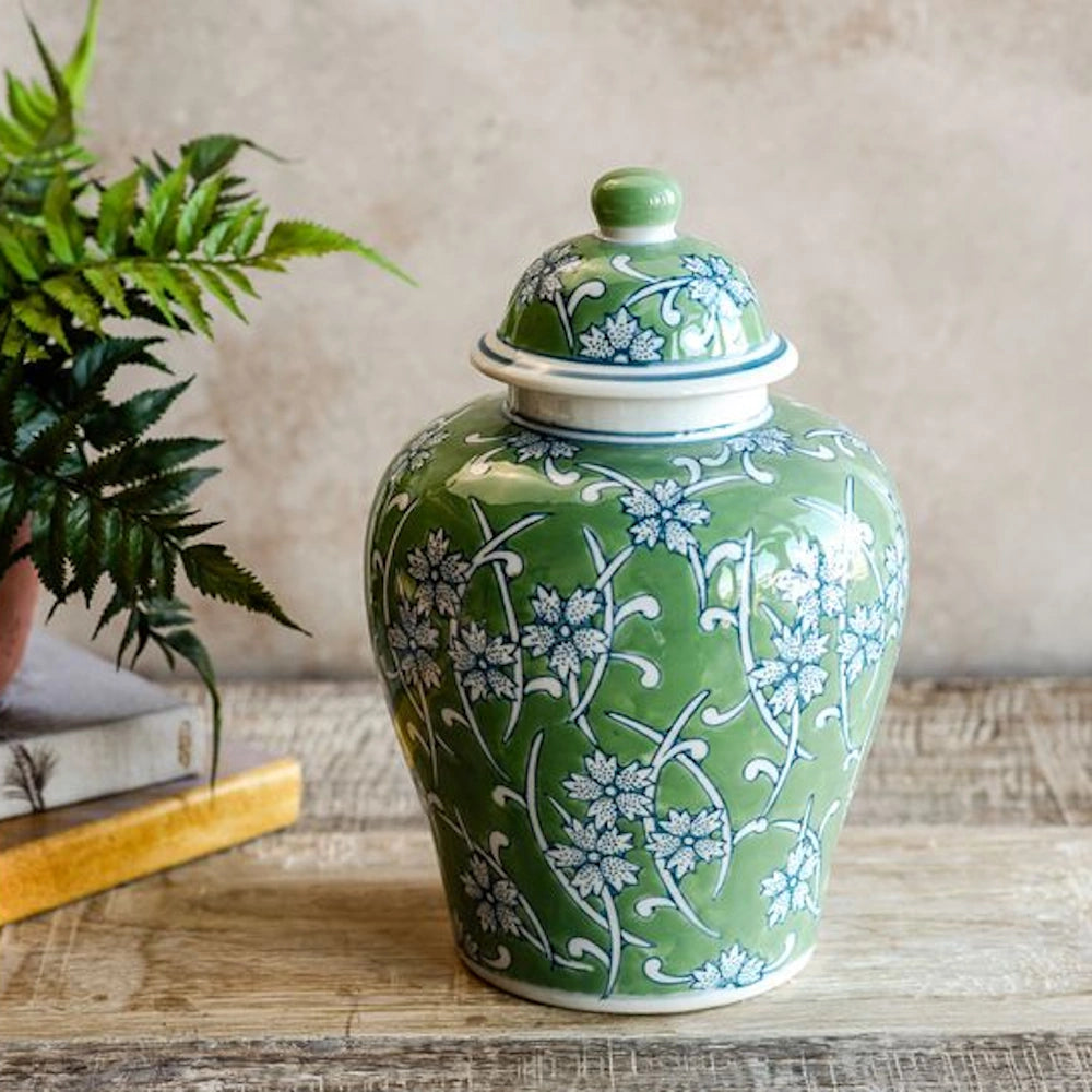 Green ceramic ginger jar with blue and white floral patterns and matching lid on a rustic wooden table.