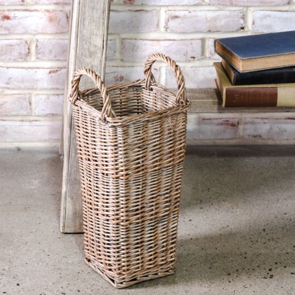 Tall grey woven willow basket with handles sitting on the floor beside vintage books.