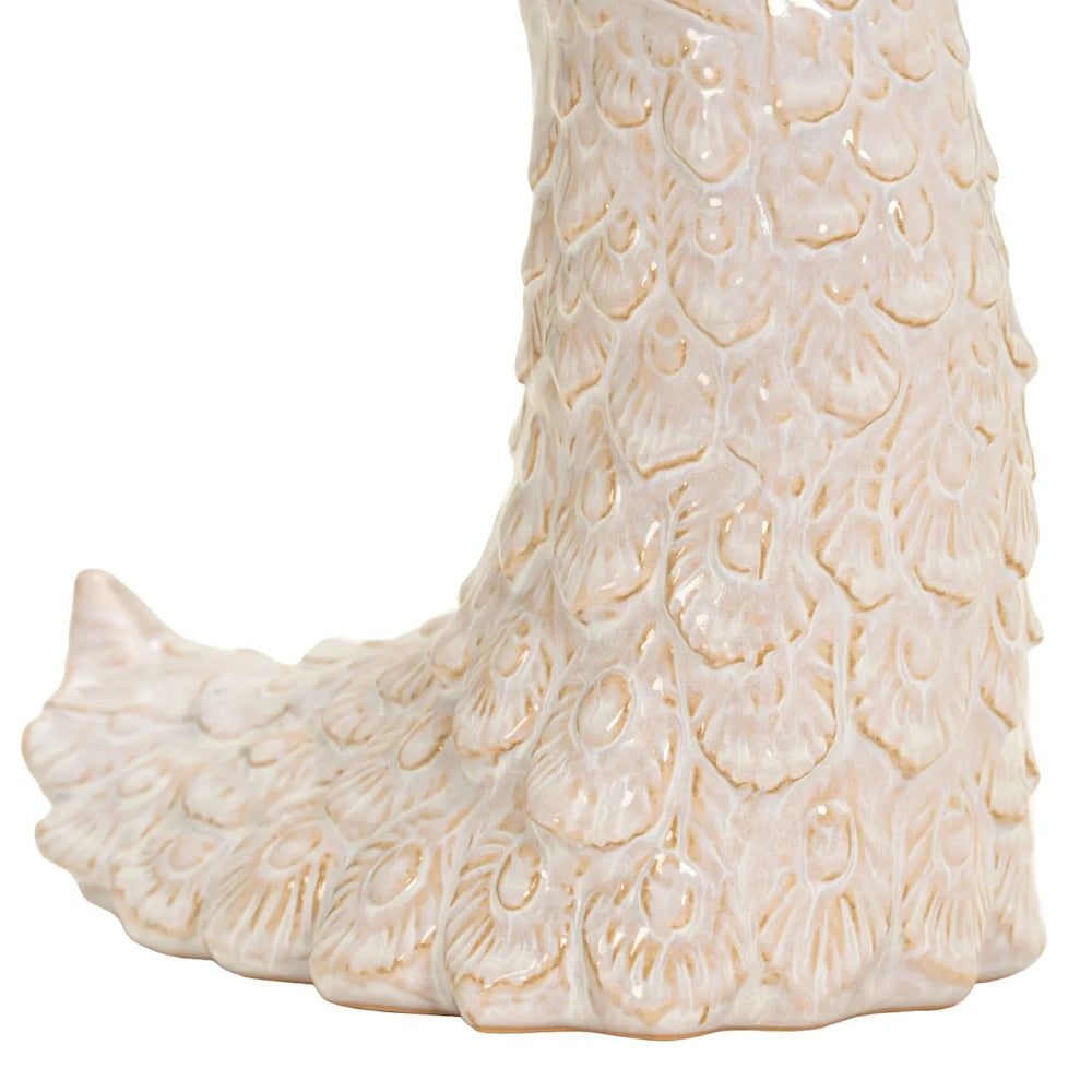 Close-up of an ivory ceramic peacock sculpture showing detailed feather textures with gold trim along the base.