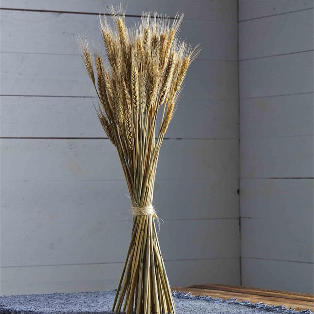 A tall bundle of dried golden wheat stalks tied with twine, standing on a blue textured mat.