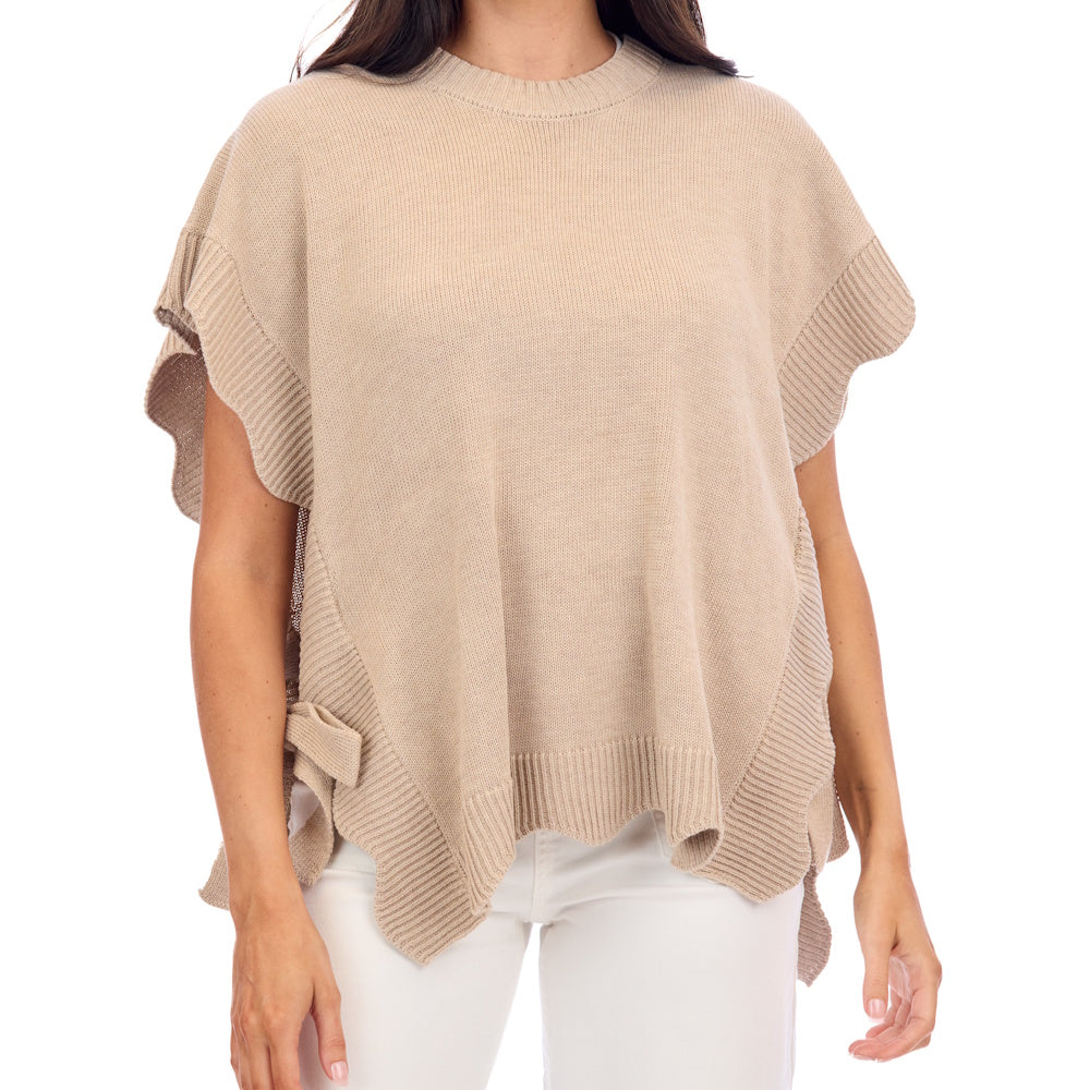 A person wearing a tan, oversized knit sweater with scalloped ribbed edges and white pants.
