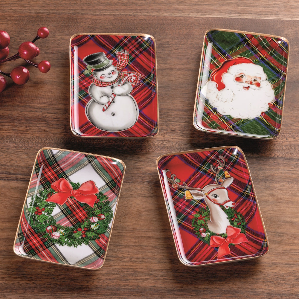 Set of four Christmas tidbit trays with holiday designs arranged on a wooden table with red berries.
