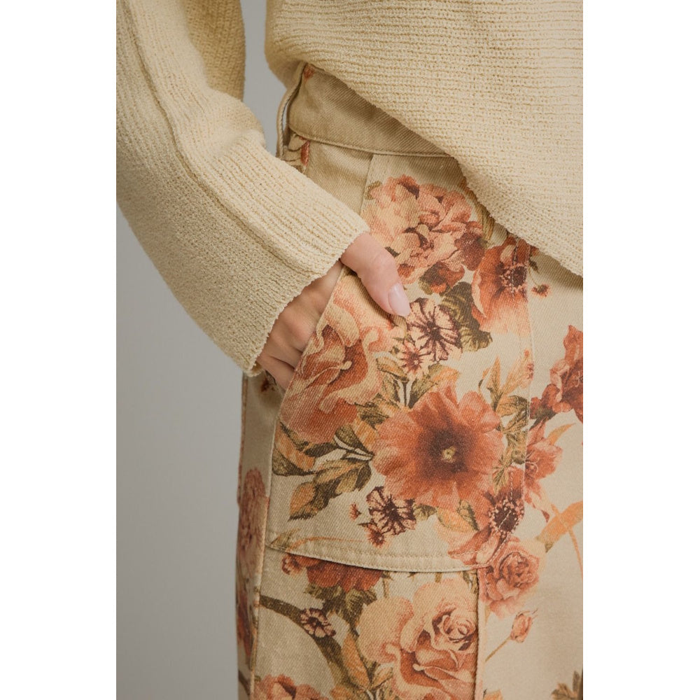 Close-up view of taupe floral print wide-leg pants highlighting a front patch pocket with a hand in it.