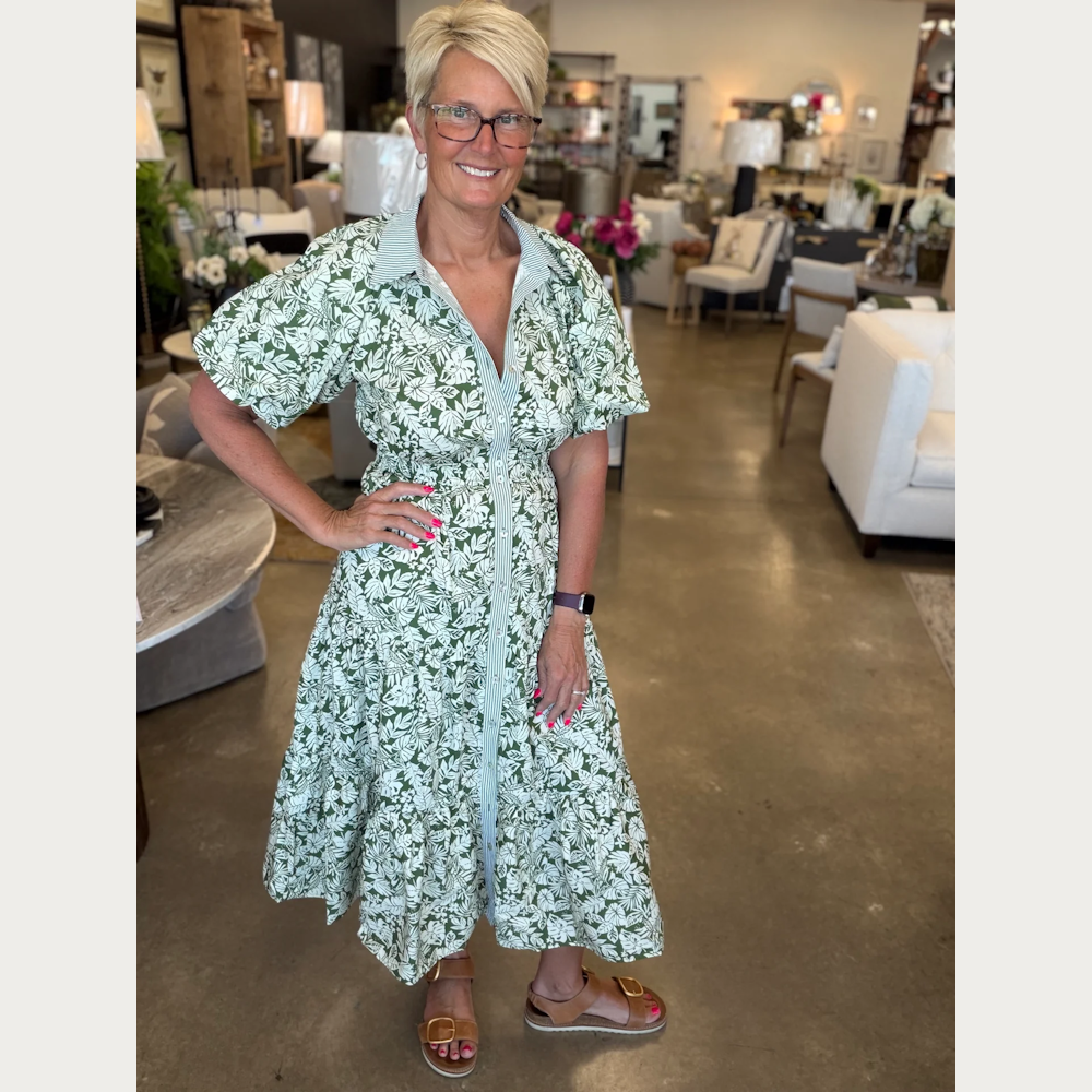 Woman in a green and white leaf print midi shirt dress with bubble sleeves and tiered skirt, posing in a furniture store.