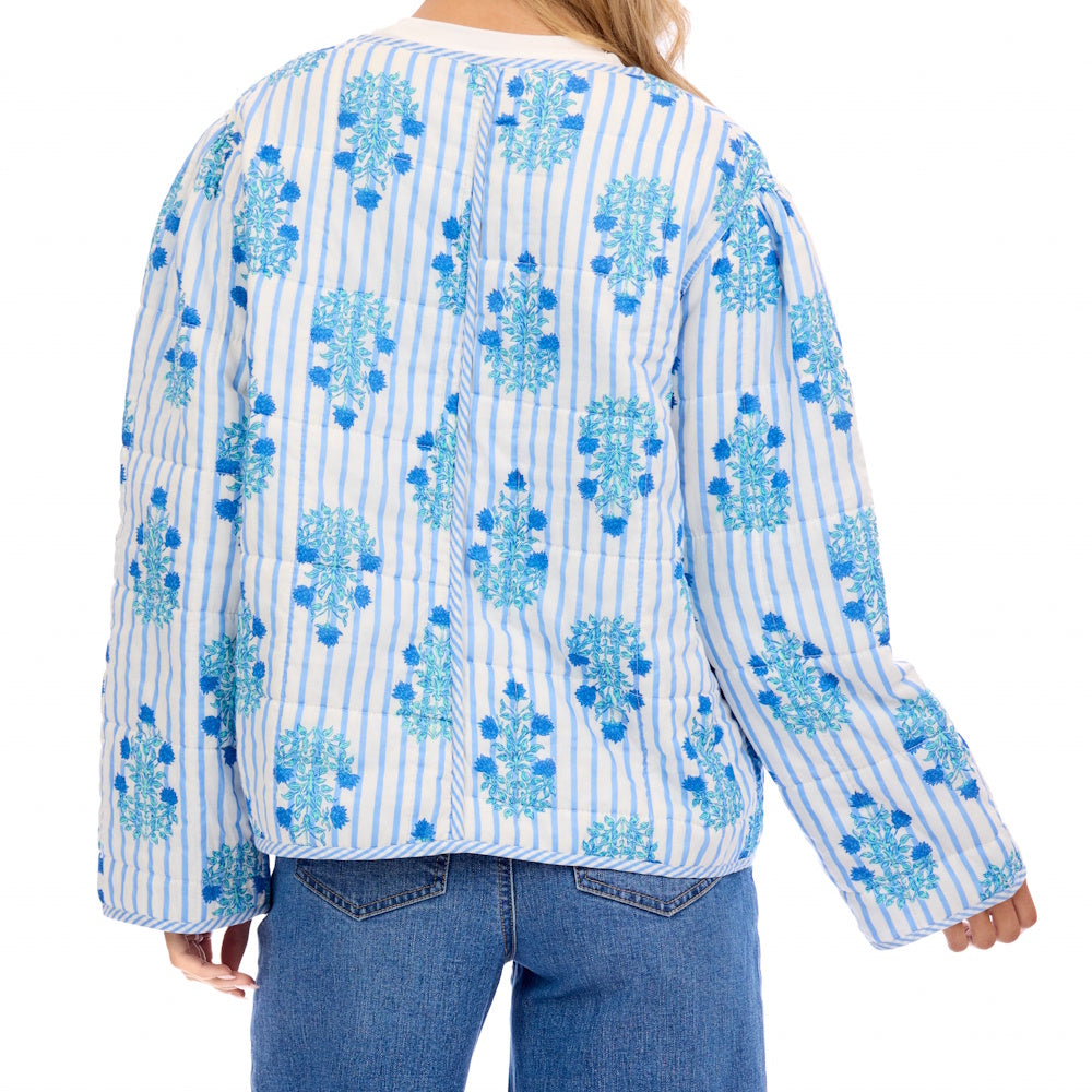 Back view of a woman wearing a blue and white striped quilted jacket with floral block prints and wide sleeves.