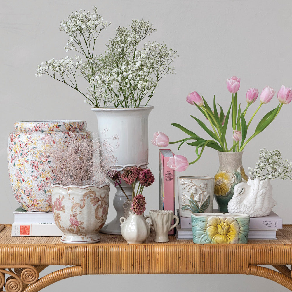 Decorative ceramic vases and planters filled with pink tulips and baby's breath on a rattan table.
