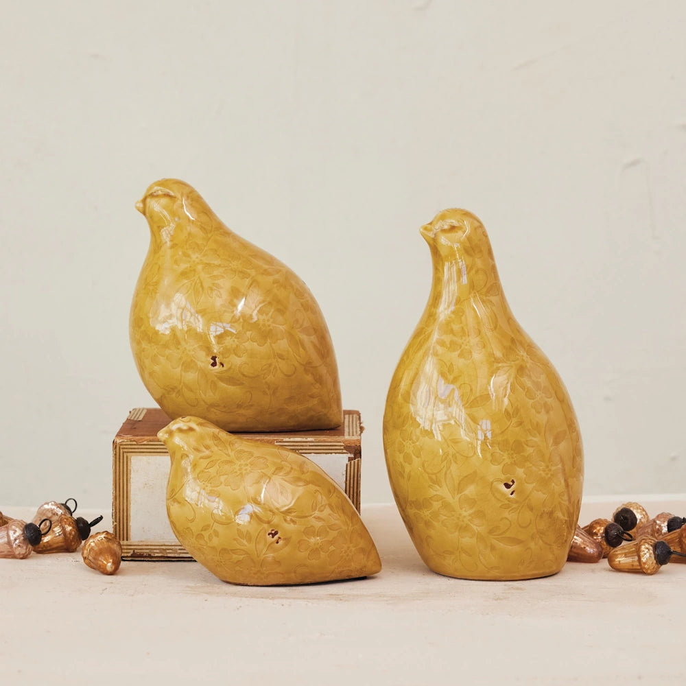 Set of three mustard yellow glazed ceramic quail figurines with floral patterns.