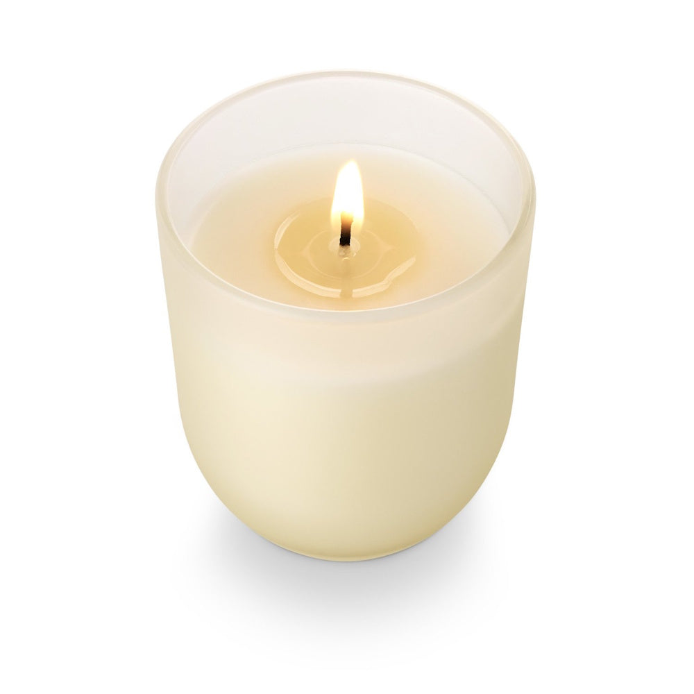 Lit white scented candle in a frosted glass jar on a white background.