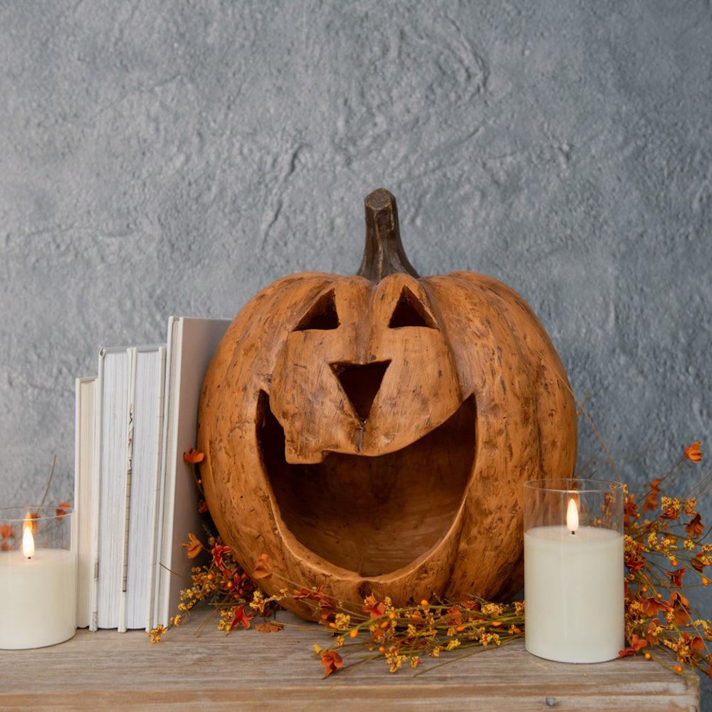 Carved terracotta jack-o'-lantern display with lit candles and books against a textured wall.