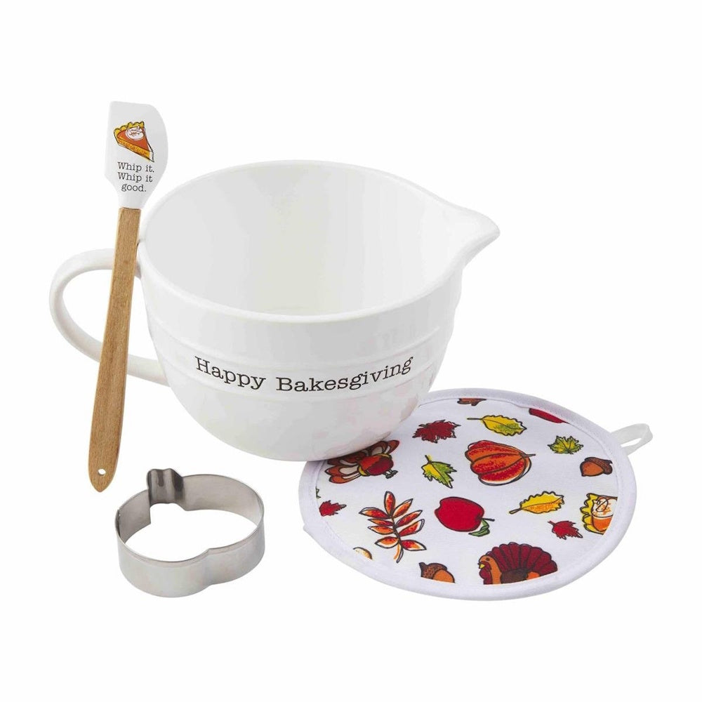 White mixing bowl set with a spatula, metal pumpkin cookie cutter, and autumn-patterned potholder.