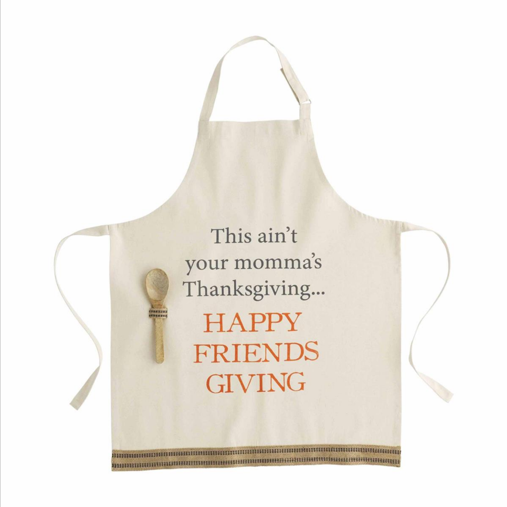 Beige apron printed with "HAPPY FRIENDSGIVING" and a small wooden spoon tucked in a pocket.
