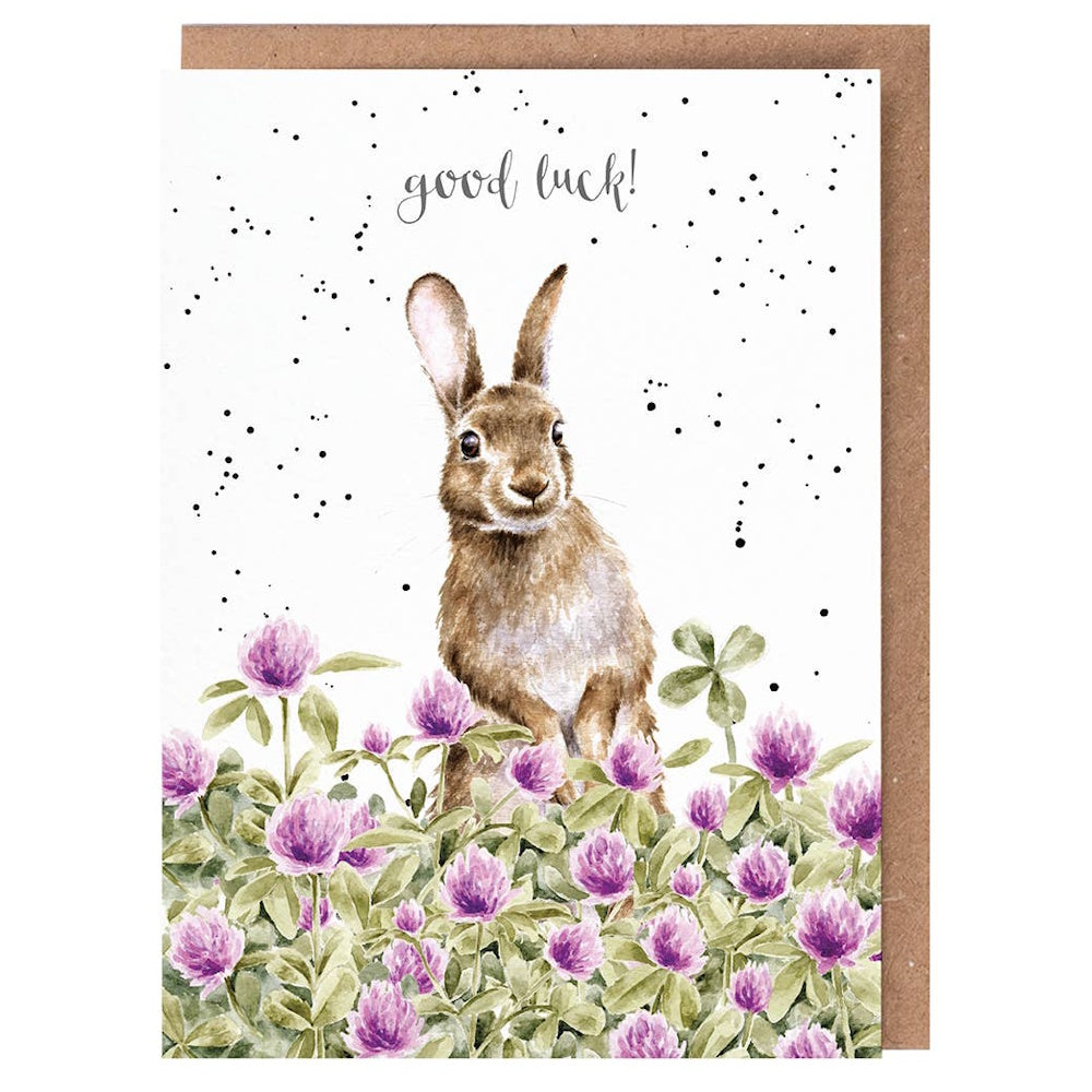 Watercolor illustration of a brown rabbit in a field of purple clover flowers with "good luck!" text and a brown envelope.