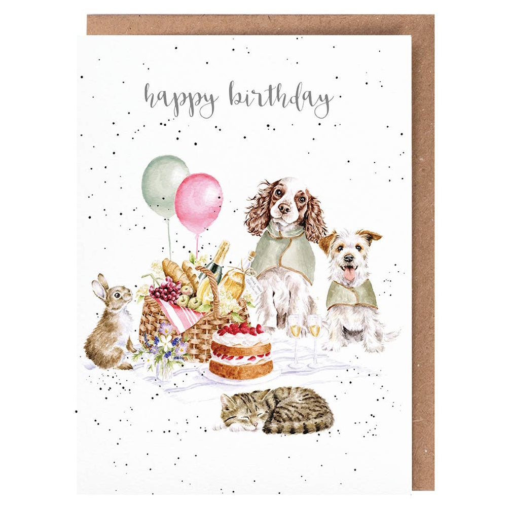 Whimsical birthday card featuring a picnic with two dogs, a rabbit, a sleeping cat, cake, and balloons on a white background.