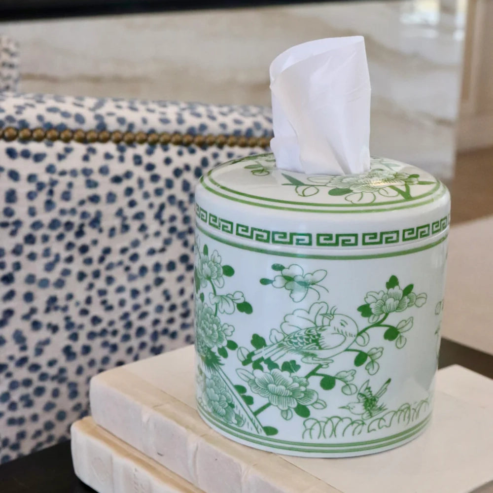 Green and white Chinoiserie ceramic round tissue box cover with floral and bird motif on decorative books.