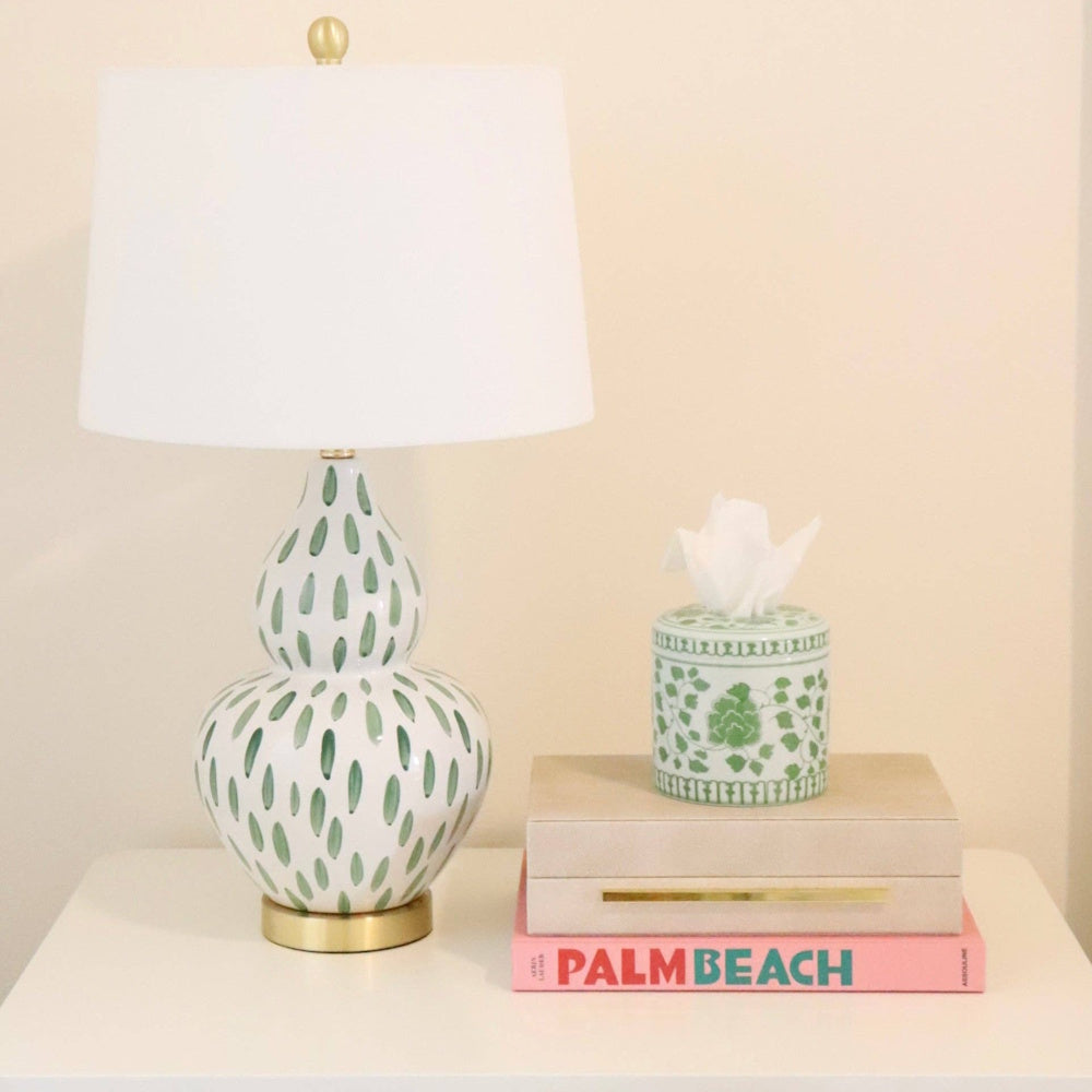Green and white floral tissue vessel next to a matching patterned lamp on a book.