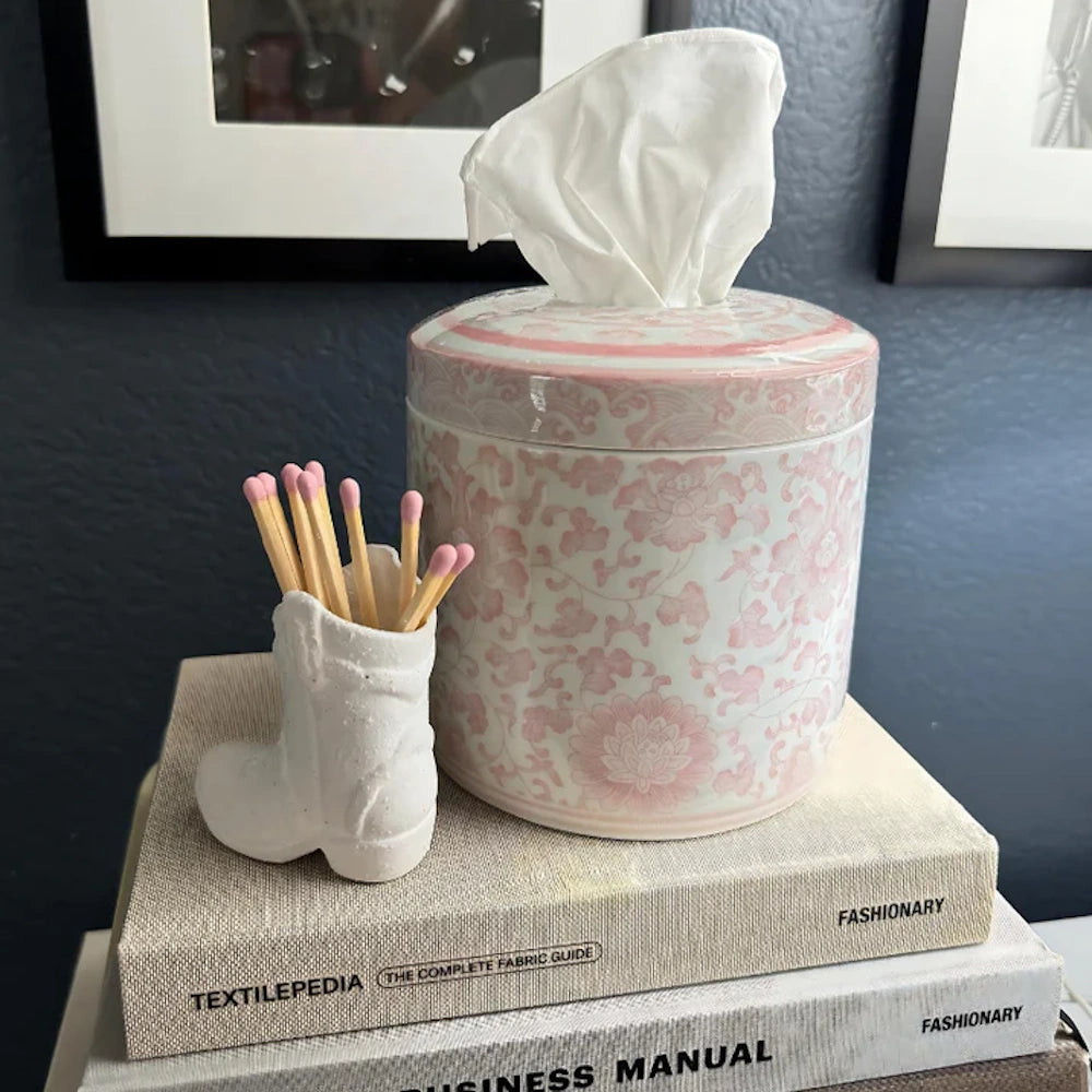 Pink floral ceramic tissue canister and a small white boot match holder sitting on top of stacked books.