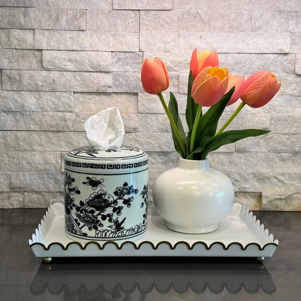 Blue and white Chinoiserie ginger jar tissue holder and white tulip vase on a scalloped tray against a stone wall.