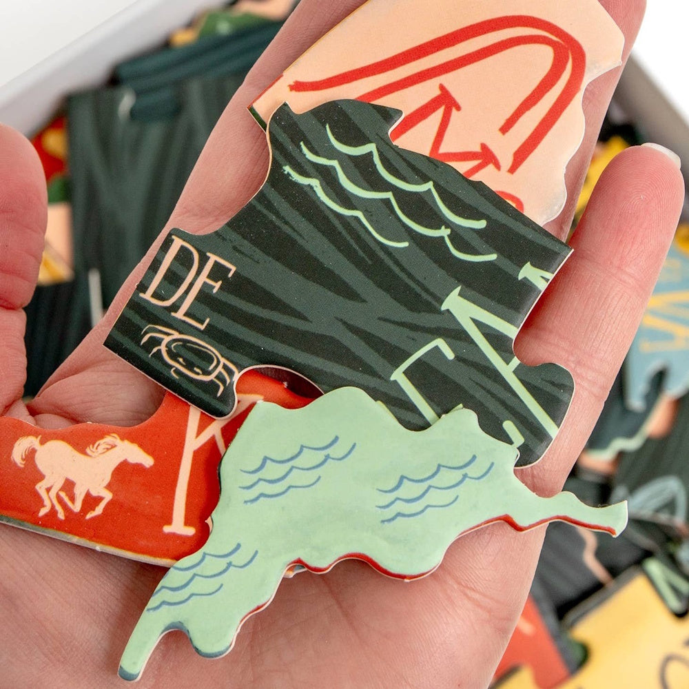 A person's palm holding several colorful, illustrated puzzle pieces in the shapes of various U.S. states.