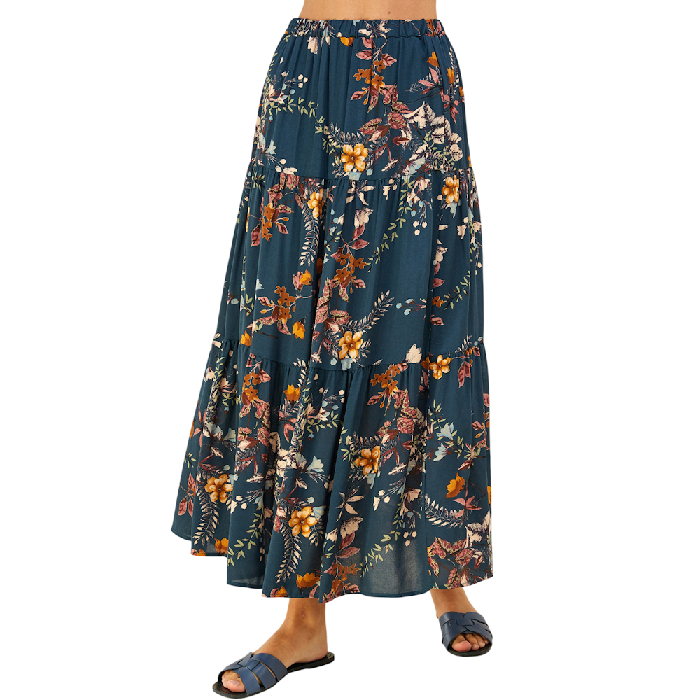 A person wearing a three-tiered floral maxi skirt in teal blue, paired with matching flat leather sandals.