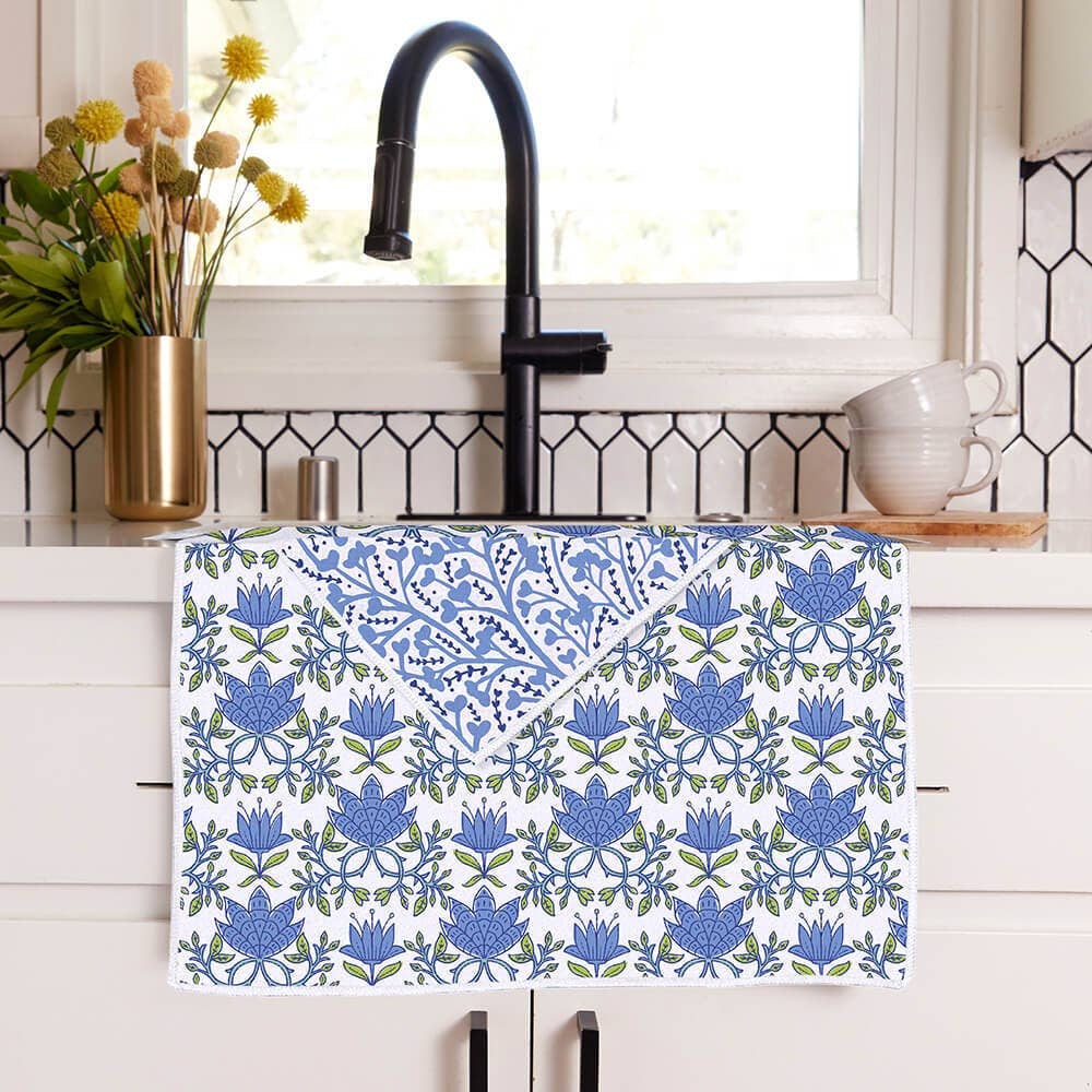 Blue and green floral pattern tea towel draped over a white kitchen counter in front of a black sink faucet.