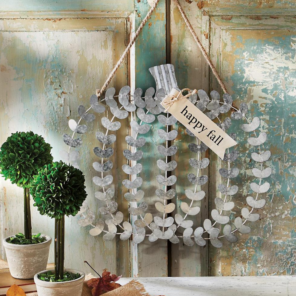 Galvanized metal leaf-patterned pumpkin door hanger with a "happy fall" tag on rustic door.